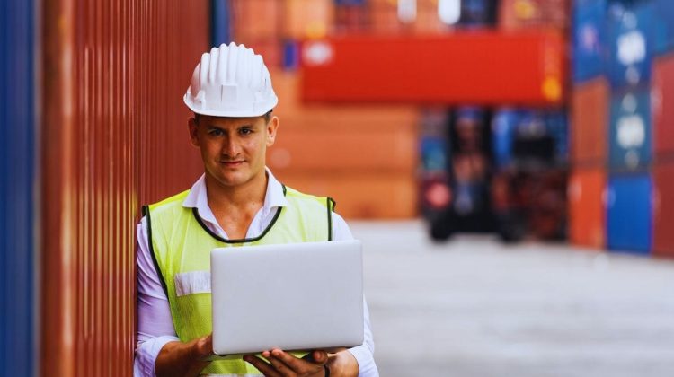 Operador logístico sosteniendo notebook en depósito de contenedores