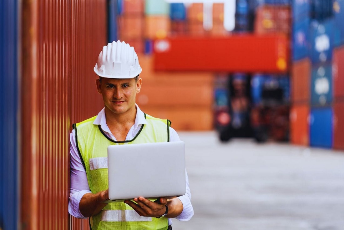 Operador logístico sosteniendo notebook en depósito de contenedores