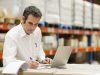 Despachante de aduana revisando documentación de importación junto a mercadería en depósito, con notebook abierta para gestión de despacho